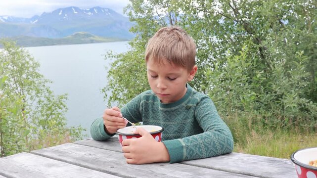 Children, boy brothers, having lunch in a reststop in Norway in beautiful nature. Kid with teddy bear eating lunch on a public wooden bench while on camping holiday in Norway
