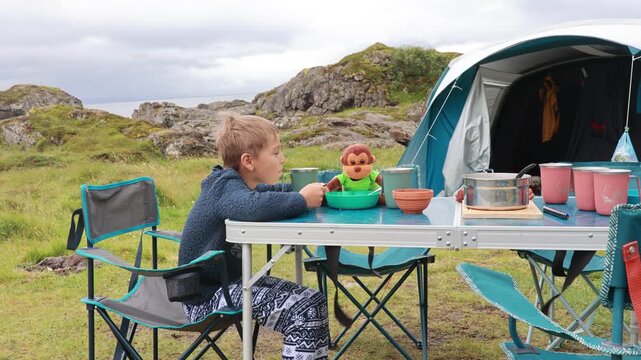 Children, boy brothers and pet dog, having breakfast in nature while wild camping in Moskenesoya, Lofoten summertime