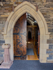 Naklejka premium Ornate wooden church door standing open within a pointed Gothic stone arch, with the historic interior visible beyond the entrance.
