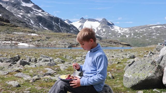 Child, eating lunch before starting the hiking of Kyrkja mountain on a beautiful sunny summer day, sunset, snow, lakes, valley