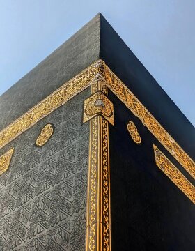 Low angle perspective of the corner of the Kaaba showing intricate Arabic calligraphy embroidered in gold thread on black silk Kiswah cloth.