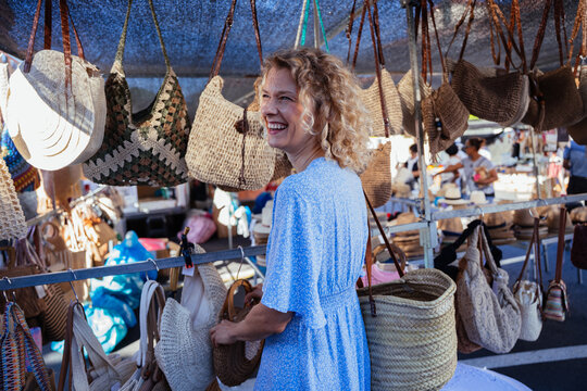 Smiling Mature Woman Shopping for Handmade Bags at Traditional Outdoor Market in Spain