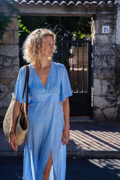 Vertical Mature Woman Walking with Woven Basket on Sunny Street in Traditional Spanish Town