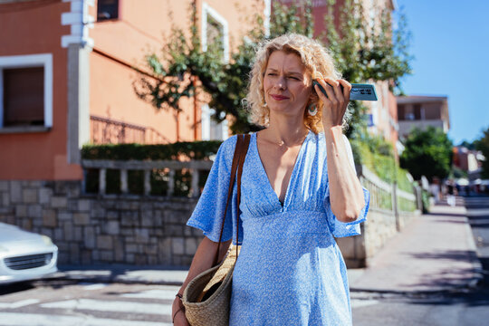 Mature Woman Listening to Smartphone Outdoors on Sunny Street in Traditional Spanish Town