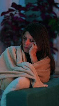 Exhausted woman dozes beneath a blanket on the living room sofa, closing her eyes before waking again and struggling with persistent tiredness, fatigue and sleepiness