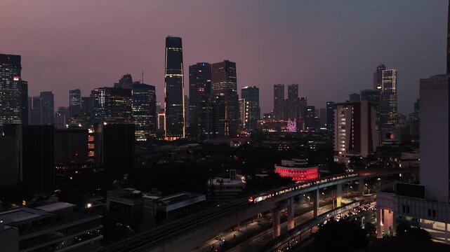 Jakarta, Indonesia - 23 July 2026: Aerial view of the city skyline at dusk with an illuminated MRT train moving along the elevated track amidst modern skyscrapers.