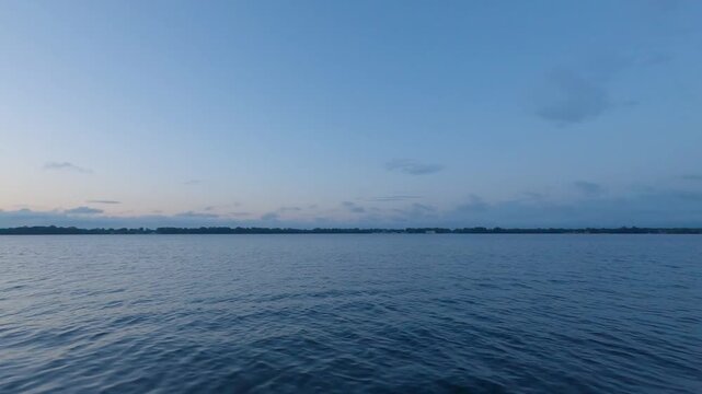 Toronto Inner Harbour facing the Toronto Islands at dawn, with calm moving water, green shoreline, and a blue sky with soft pink light.