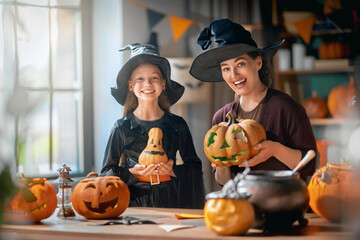 Naklejka premium Happy Mother and Daughter Carving Pumpkins in Witch Costumes for Halloween