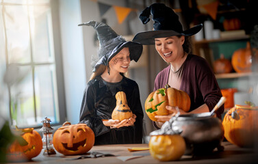 Naklejka premium Happy Mother and Daughter in Witch Costumes Carving Pumpkins