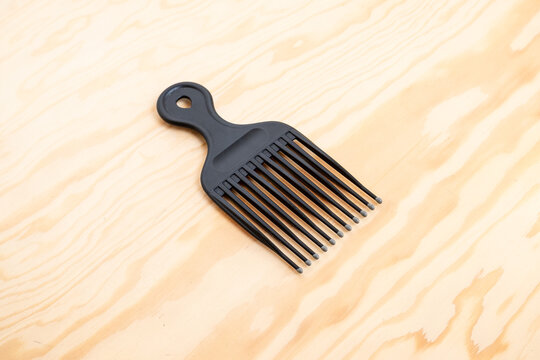 Black wide tooth hair pick lying on wooden table viewed from above
