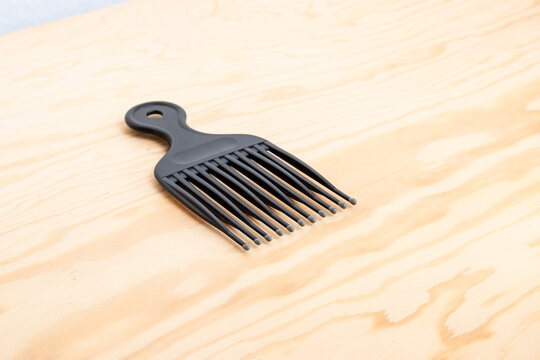 Black hair pick comb resting diagonally on wooden table
