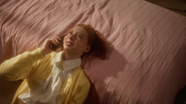 Caucasian teenage girl lying on floor next to bed, talking on cordless vintage phone and gesturing, high angle shot. Clip is suitable for telecom marketing or youth lifestyle commercials