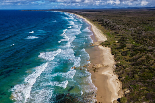 Aerial view of the long sandy shoreline of Sand Dune Beach at Brooms Head, featuring clear turquoise water, coastal dunes and surrounding natural landscape along the Clarence Valley coastline
