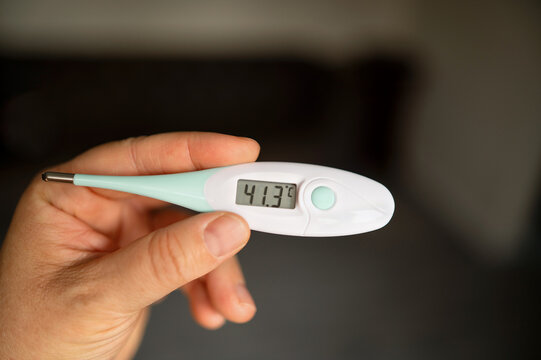 Close-up of hand holding a digital thermometer at home. concept: healthcare, illness, and monitoring temperature.