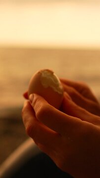 Egg peeling sunset hands peeling a hard boiled egg against a golden sea background during an outdoor picnic