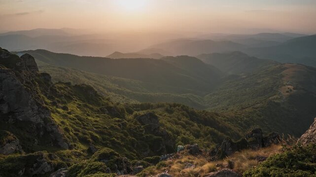 Timelapse of warm golden light during sunset over endless mountain ridges and deep forest valleys viewed from Babin Zub peak on Stara Planina, Serbia. Cinematic nature landscape.
