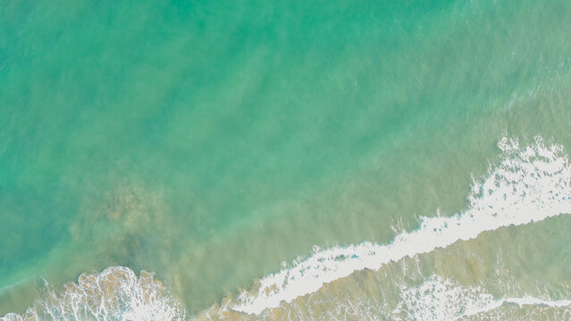 Aerial top down view of turquoise clear sea water surface with light white waves foam moving over sandy seabed texture horizontal stock photo