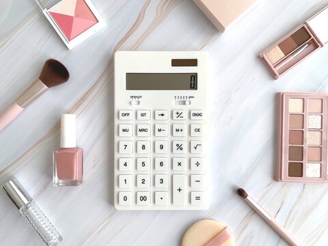 白い電卓とピンク系コスメのフラットレイ背景／化粧品の価格・予算イメージ
