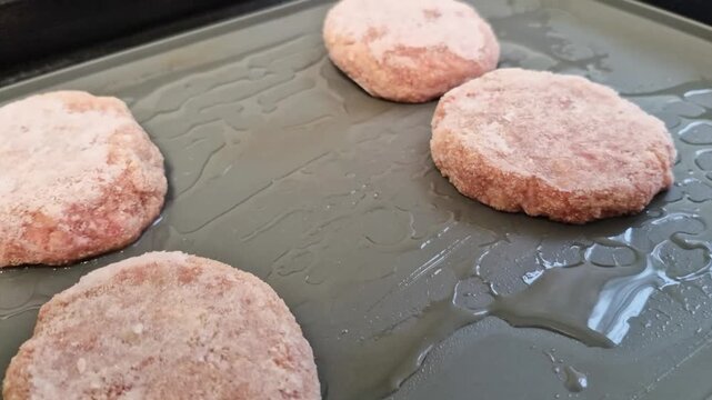 Raw meat patties on oiled tray ready for baking in kitchen