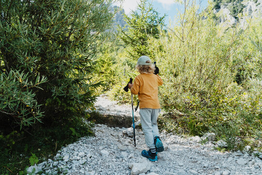 Little boy with hiking poles walking on rocky mountain path. Healthy active family lifestyle and safe summer camping concept.