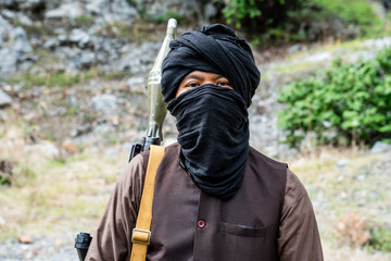 Naklejka premium Masked figure stands with rifle in mountainous terrain during daytime