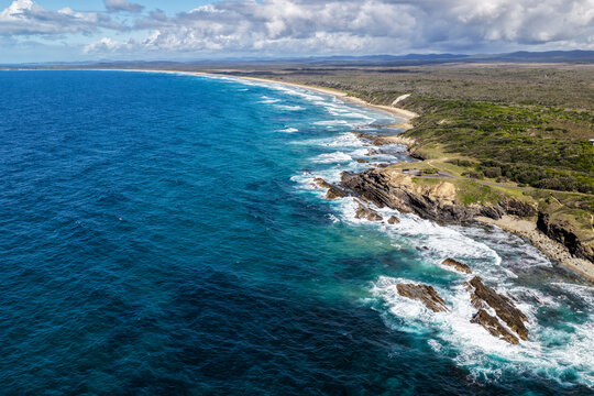 Aerial view of the Brooms Head headland surrounded by the Pacific Ocean, with the long sandy shoreline of Sand Dune Beach stretching along the coast and surrounding natural landscape