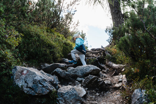 Cute little boy carefully climbing large rocks on steep mountain path. Happy safe childhood and active family nature travel.
