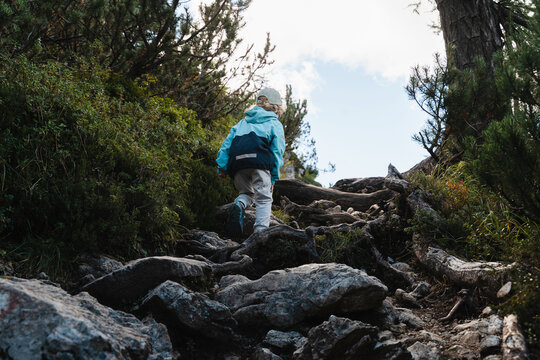 Cute little boy carefully climbing large rocks on steep mountain path. Happy safe childhood and active family nature travel.