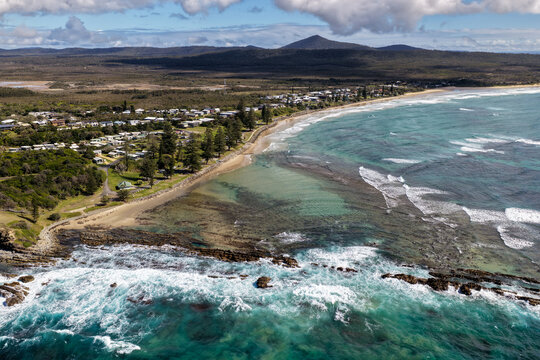 Aerial view of Brooms Head Beach and the coastal rockpool, with the township of Brooms Head visible in the background, showcasing the sandy shoreline, Pacific Ocean and surrounding coastal landscape 