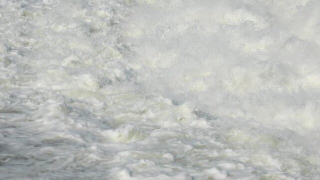 Slow motion view of dark green river water merging into white foamy currents, creating deep whirlpool swirls and strong surface turbulence downstream.
