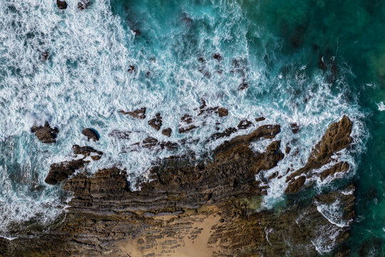 Aerial downward view of ocean waves crashing over the rugged rocky coastline at Brooms Head, capturing white surf, exposed rock formations and surrounding Pacific Ocean along the Clarence Valley 