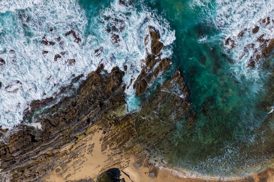Aerial downward view of ocean waves crashing over the rugged rocky coastline at Brooms Head, capturing white surf, exposed rock formations and surrounding Pacific Ocean along the Clarence Valley 