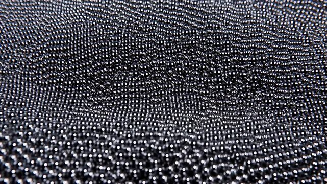 Dense field of small metallic spheres oscillates to form dynamic undulating wave patterns on a dark surface. Animated backdrop combines specular highlights with visible depth.