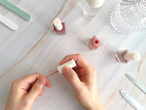 爪にマニキュアを塗る女性の手と机上のネイルケアアイテム