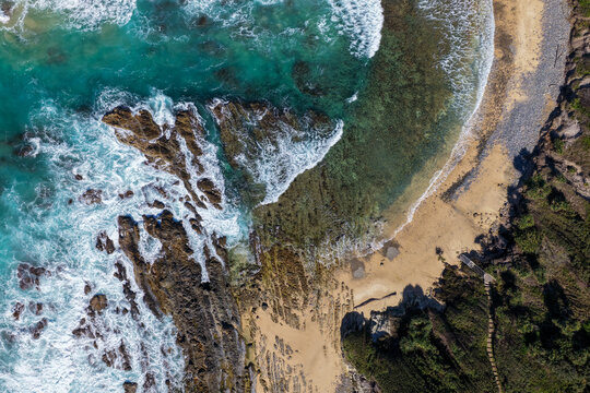 Aerial downward view of ocean waves crashing over the rugged rocky coastline at Brooms Head, capturing white surf, exposed rock formations and surrounding Pacific Ocean along the Clarence Valley