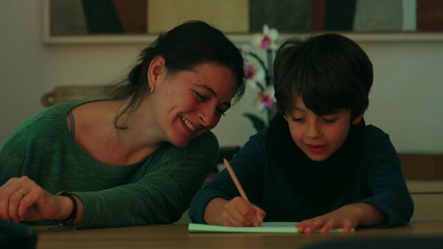 Smiling mother encourages her son as he completes a writing exercise at the family table, celebrating educational progress, shared learning and joyful connection