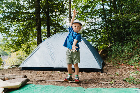 Cheerful young boy standing with arms raised near a campsite tent celebrating outdoor freedom.