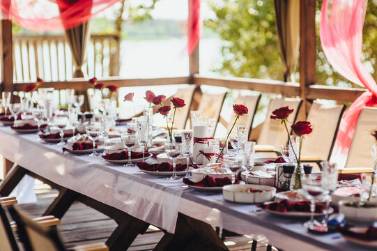 Photo of a banquet, buffet table setting in a restaurant, red flowers, roses, dishes and food.