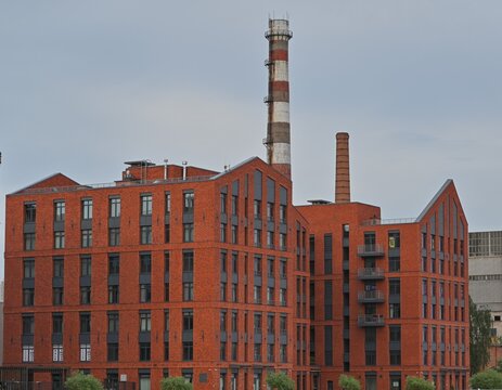 Modern red brick residential buildings stand beside industrial chimneys. Good for architecture magazines, real estate websites, urban development presentations, city planning publications