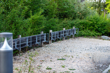 Fototapeta premium An empty wooden bicycle rack with metal holders sits beside a gravel path in a lush green park.