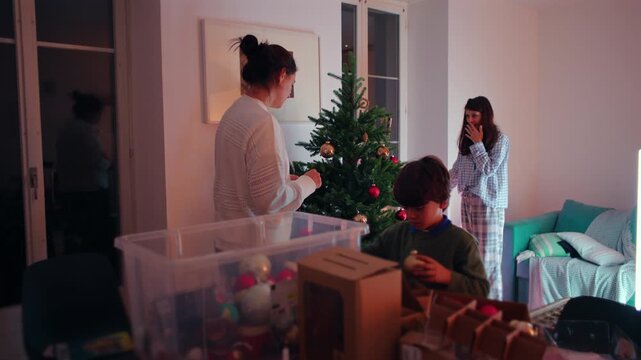 Family selects and arranges Christmas ornaments around a tree in the home living room, expressing festive anticipation, collaborative preparation and seasonal unity