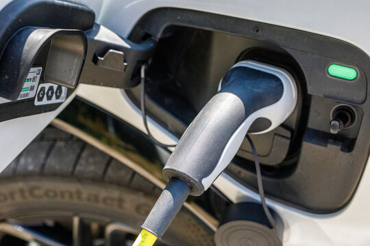Close-up of an electric vehicle charging cable plugged into a white car's port.