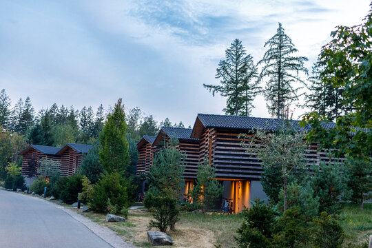 Stylish wooden cabins in a forest resort at dusk, featuring modern rustic design and warm lighting.