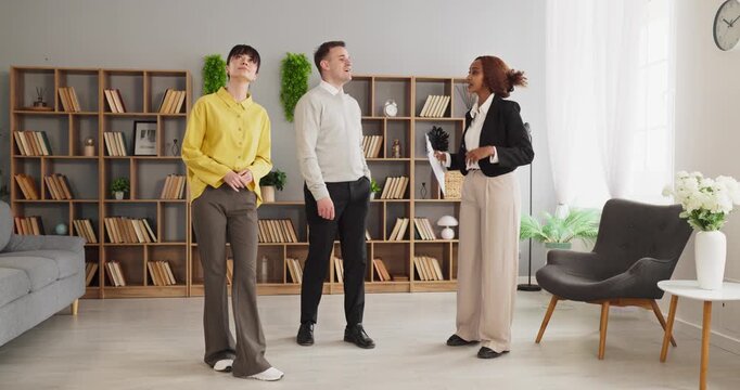 Agent and couple viewing apartment interior during tour. Agent guides buyers in a bright home, noting features, consultation and options to buy or lease. Home buying and consultation concept.
