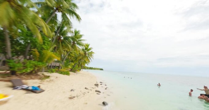 FPV aerial view of a tropical beach with yellow lounge chairs, palm trees, and people relaxing in hammocks, Fiji.