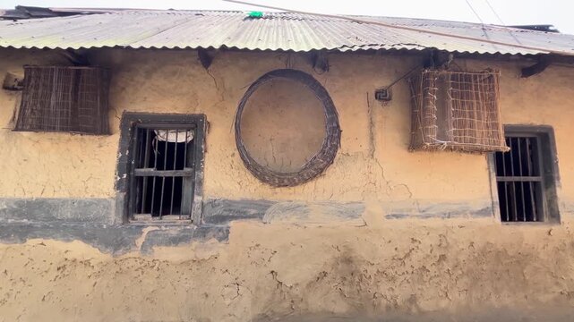 Rustic mud house exterior wall with traditional handmade circular woven storage unit and wooden barred windows.