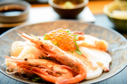 Fresh seafood donburi bowl featuring plump shrimp and glistening orange roe, elegant Japanese cuisine presentation with white ceramic dish and traditional tableware