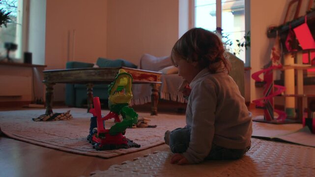 Toddler playing with colorful crocodile toy while seated on a padded floor mat in a family living room, reaching forward to touch the open green mouth indoors