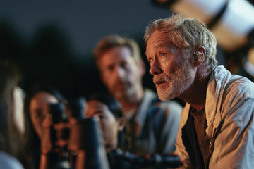 Fototapeta premium An older man passionately shares astronomy insights with a group of eager listeners under the night sky, highlighting the beauty of stargazing and learning.