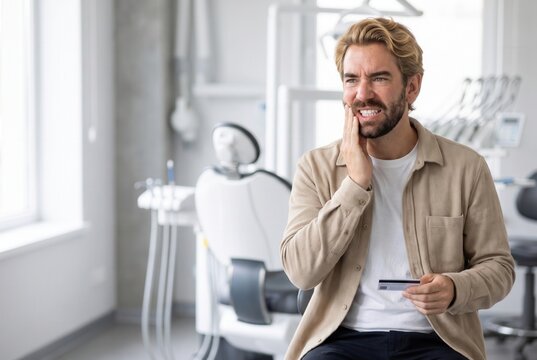 Man experiencing severe tooth pain in a dental clinic, holding a credit card